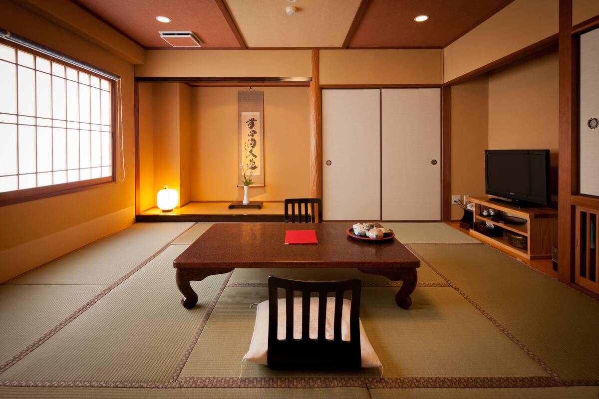 A traditional Japanese room with tatami flooring, a low table, chairs, a television, and sliding doors.
