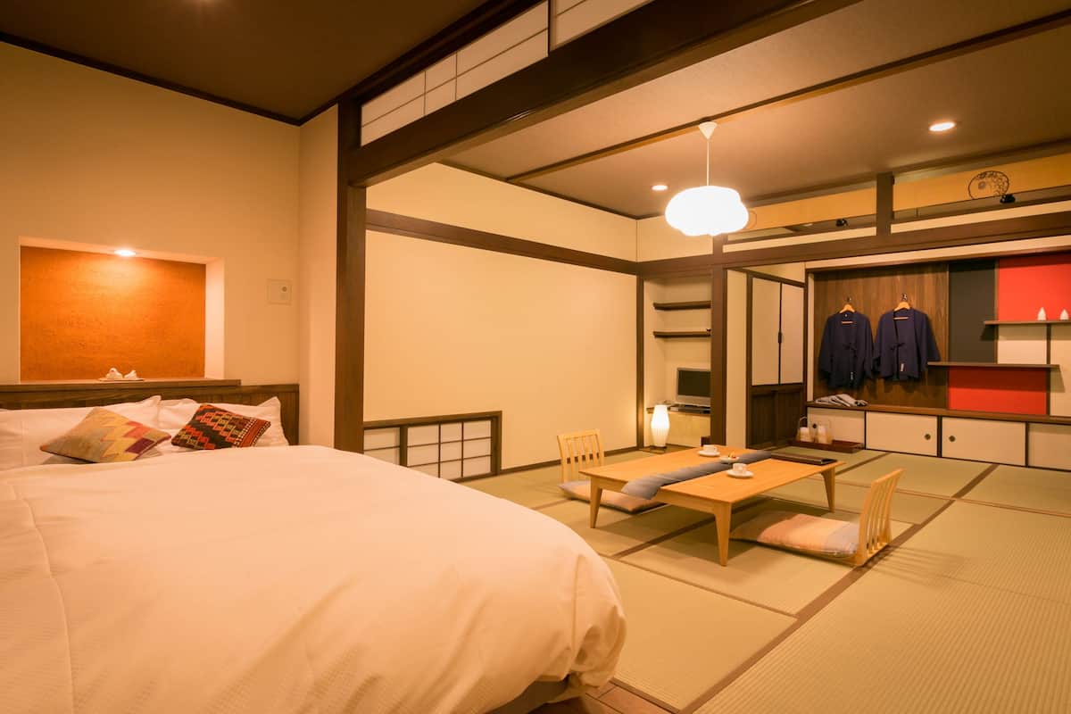 A traditional Japanese room with tatami flooring, a low wooden table, a bed with pillows, and a hanging clothing rack.
