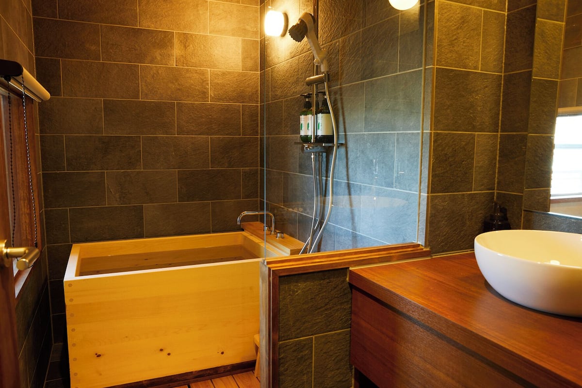 A bathroom with a wooden bathtub, a glass-enclosed shower, and a white sink.