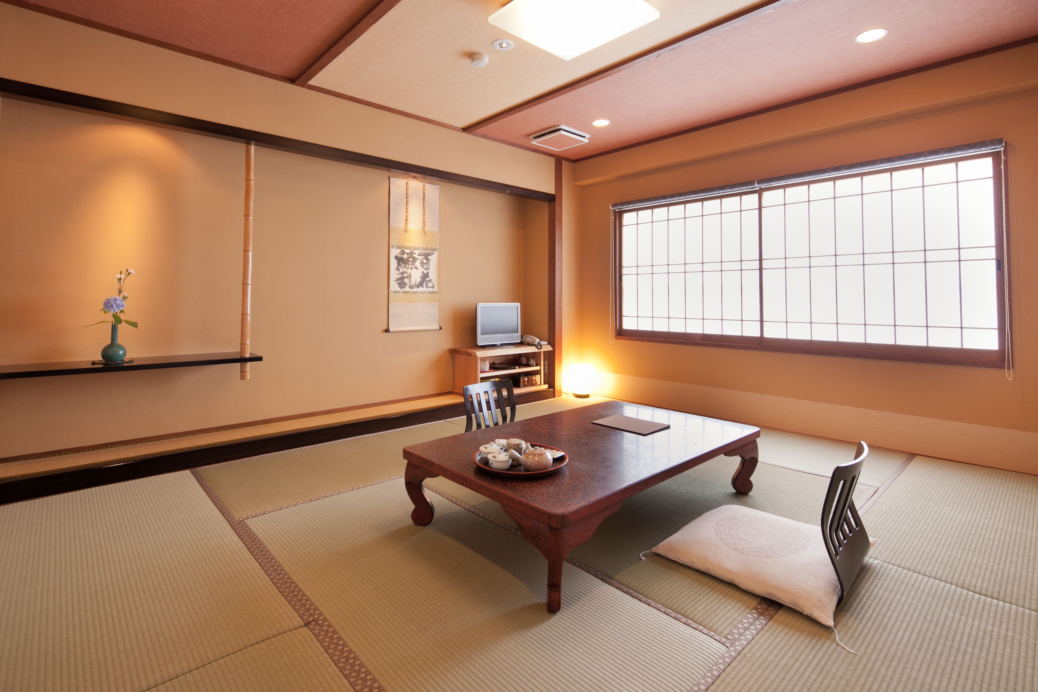 A traditional Japanese room with tatami flooring, a low table with a tea set, a television, and a large window with shoji screens.
