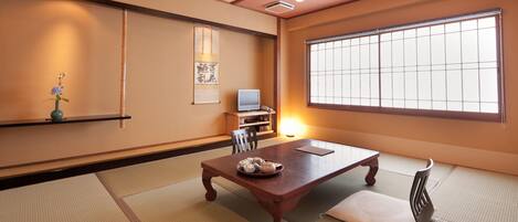 A traditional Japanese room with tatami flooring, a low table with a tea set, a television, and a large window with shoji screens.