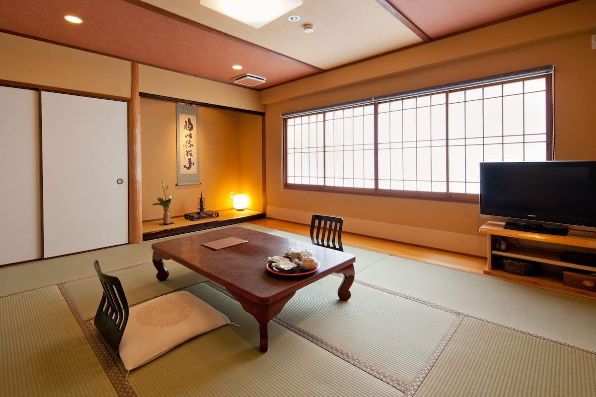 A traditional Japanese room with tatami flooring, a low table with a decorative plate, a television on a wooden stand, and a sliding door.