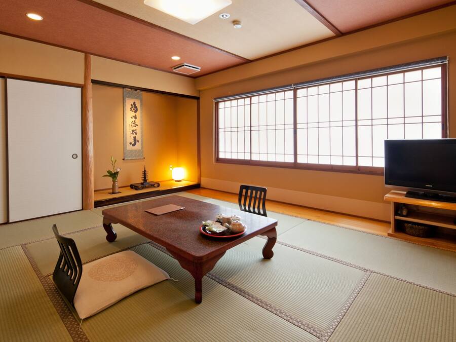 A traditional Japanese room with tatami flooring, a low table with a decorative plate, a television on a wooden stand, and a sliding door.