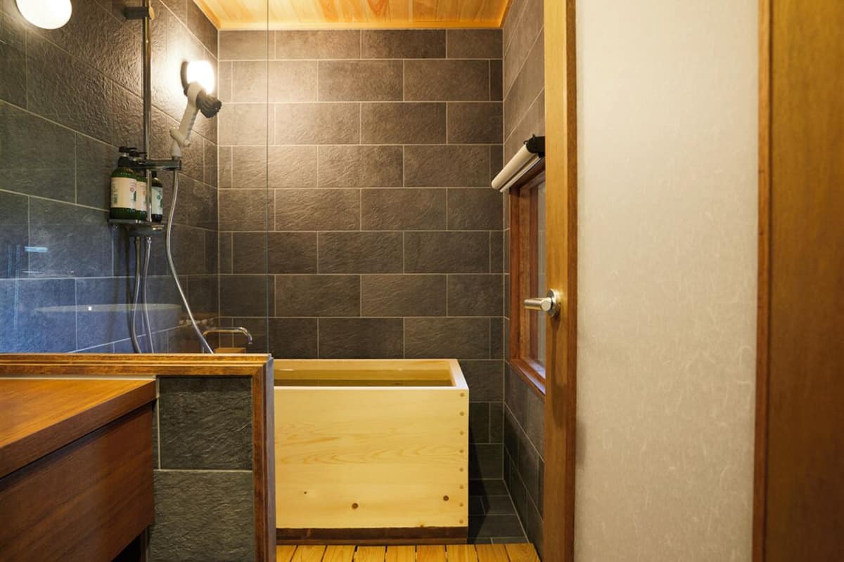 A bathroom with a shower, a wooden bathtub, and a toilet.