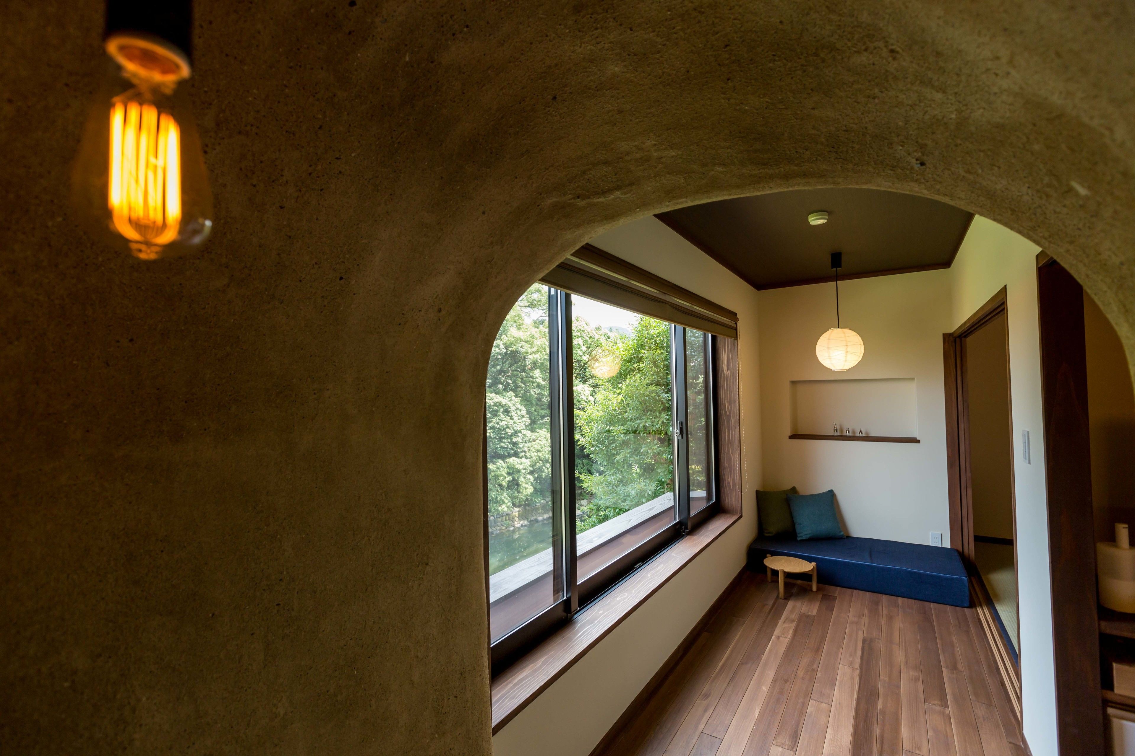 A room with a wooden floor, a bench, a window with a view of trees, and a hanging light fixture.
