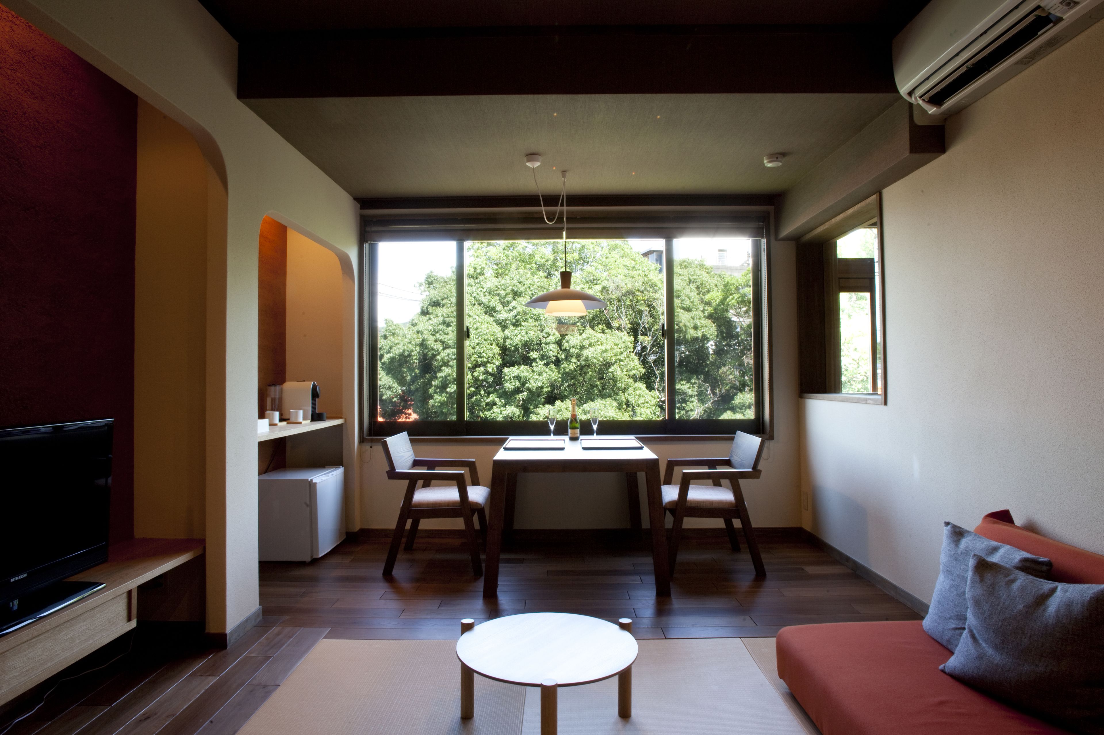 Un salon moderne comprenant un téléviseur, une table à manger avec des chaises, un canapé et de grandes fenêtres donnant sur la verdure.