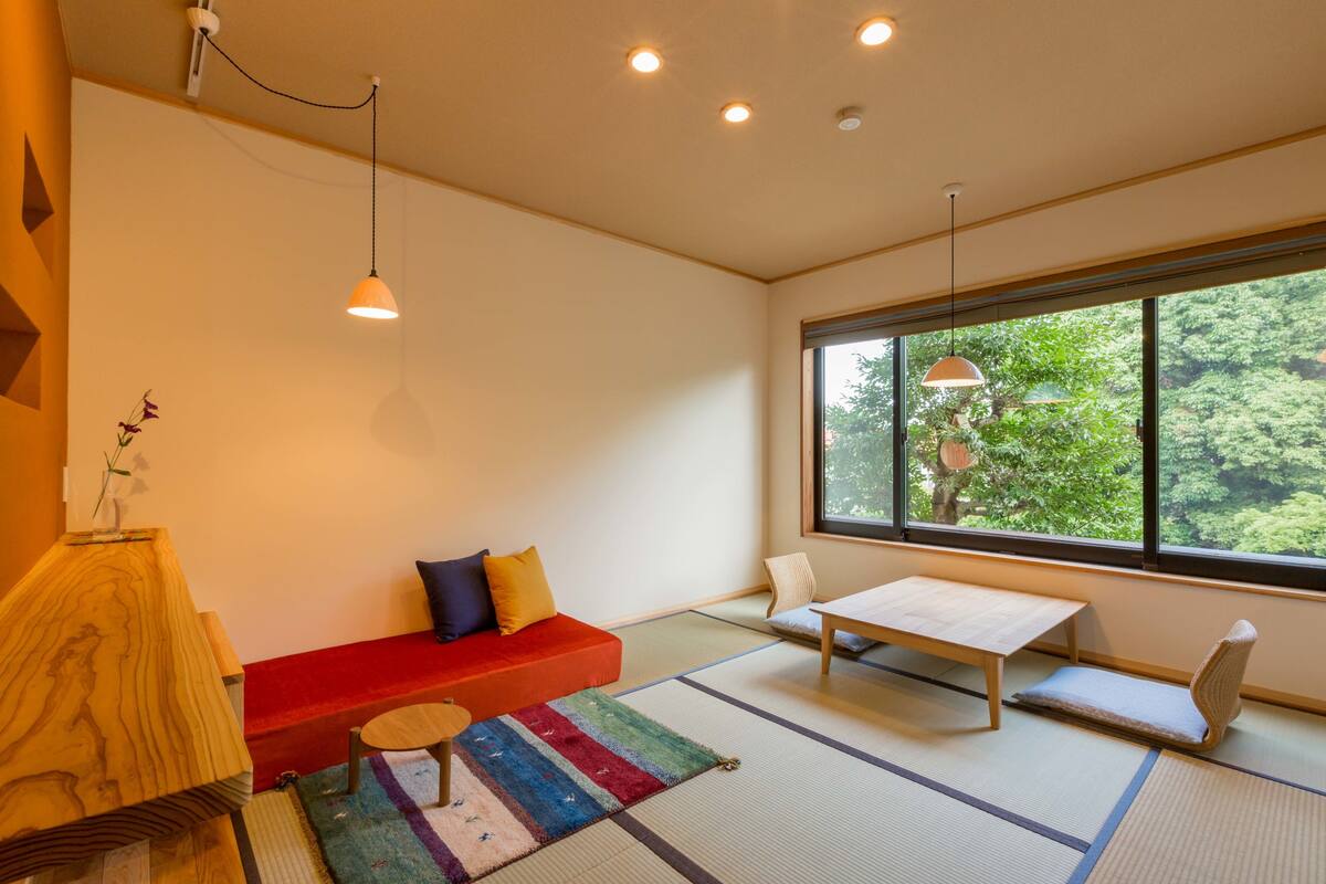 A modern room with tatami mats, a red sofa, a small table, and a view of greenery through large windows.