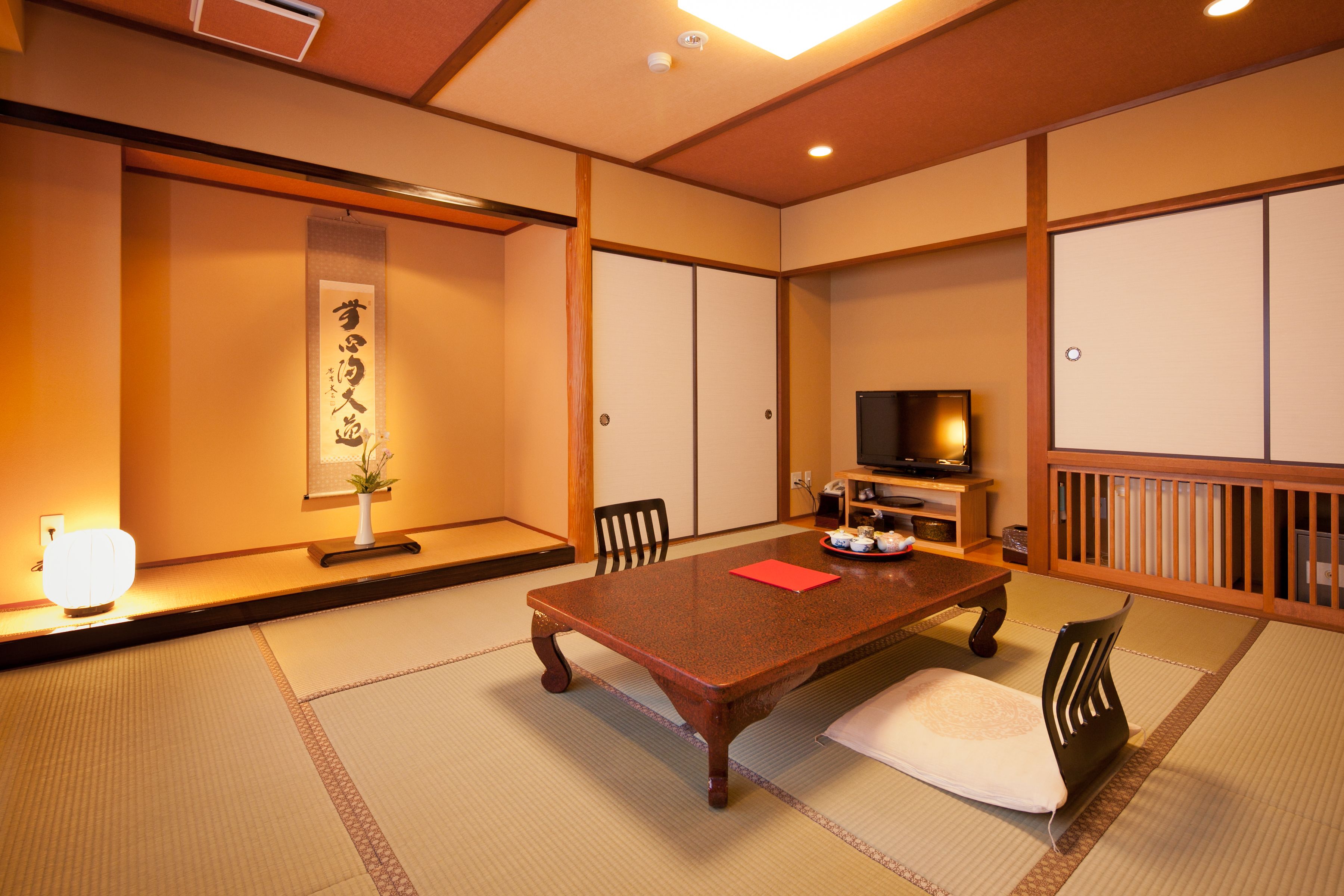 Una habitación japonesa tradicional con suelo de tatami, una mesa baja, sillas, un televisor y una puerta corredera.