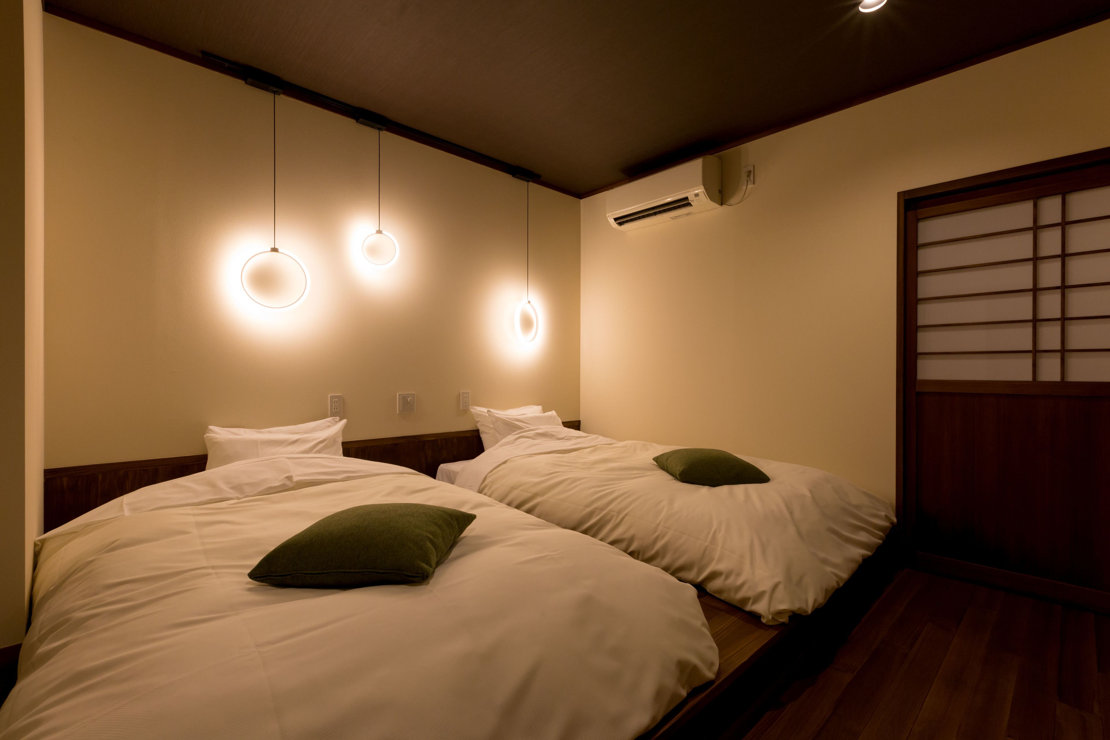 Une chambre d’hôtel avec deux lits, chacun doté de draps blancs et d’oreillers verts, d’une tête de lit en bois et d’une porte coulissante traditionnelle.