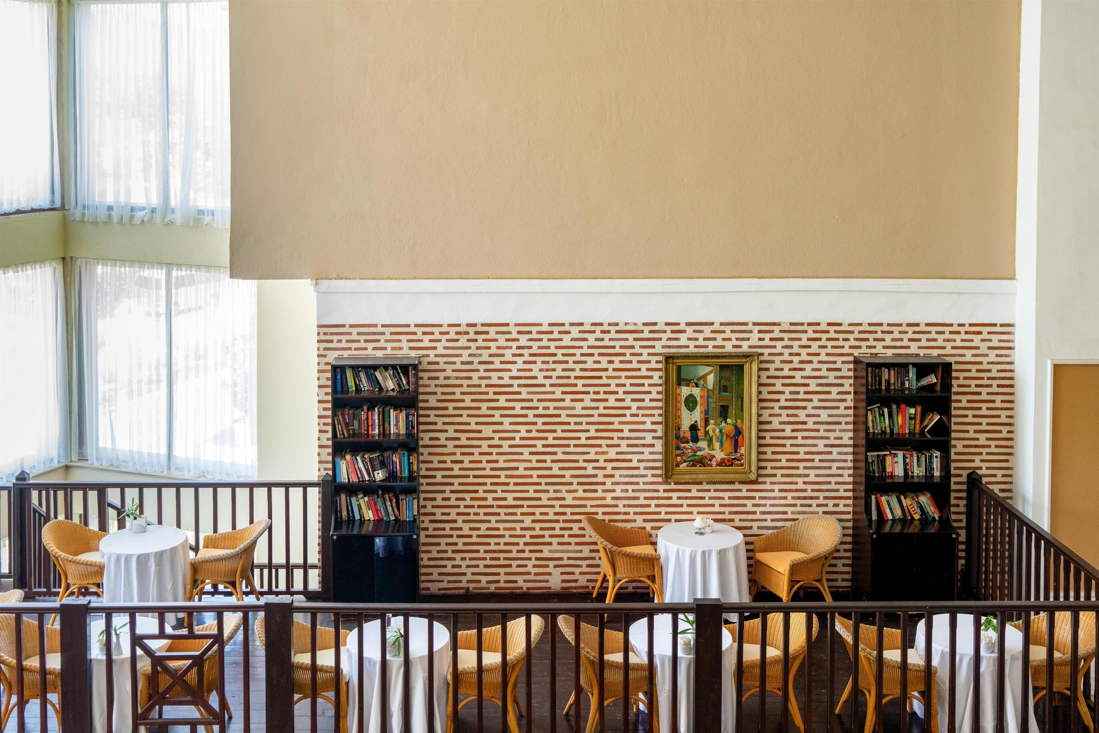 A library with brick walls, bookshelves, wicker chairs, and tables.