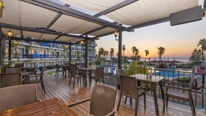 A wooden deck with wicker furniture, overlooking a pool and a sunset. - Armas Labada (Kemer)