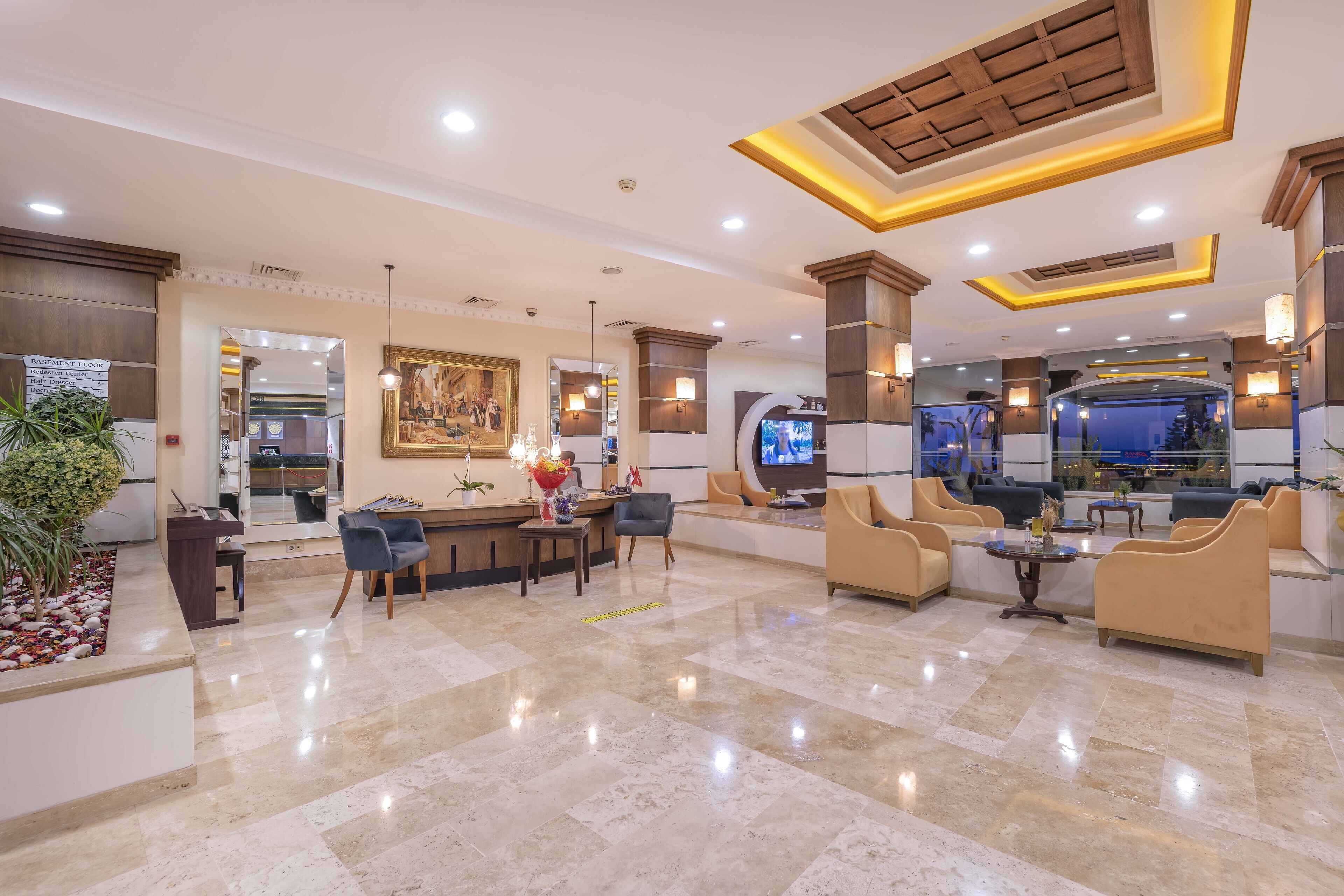 A hotel lobby with a reception desk, seating area, and a large television screen.