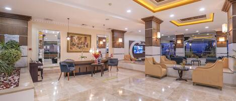A hotel lobby with a reception desk, seating area, and a large television screen.