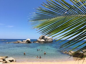 A beach with clear blue water, people swimming, and large rocks. - Poseidon Resort (Koh Tao)