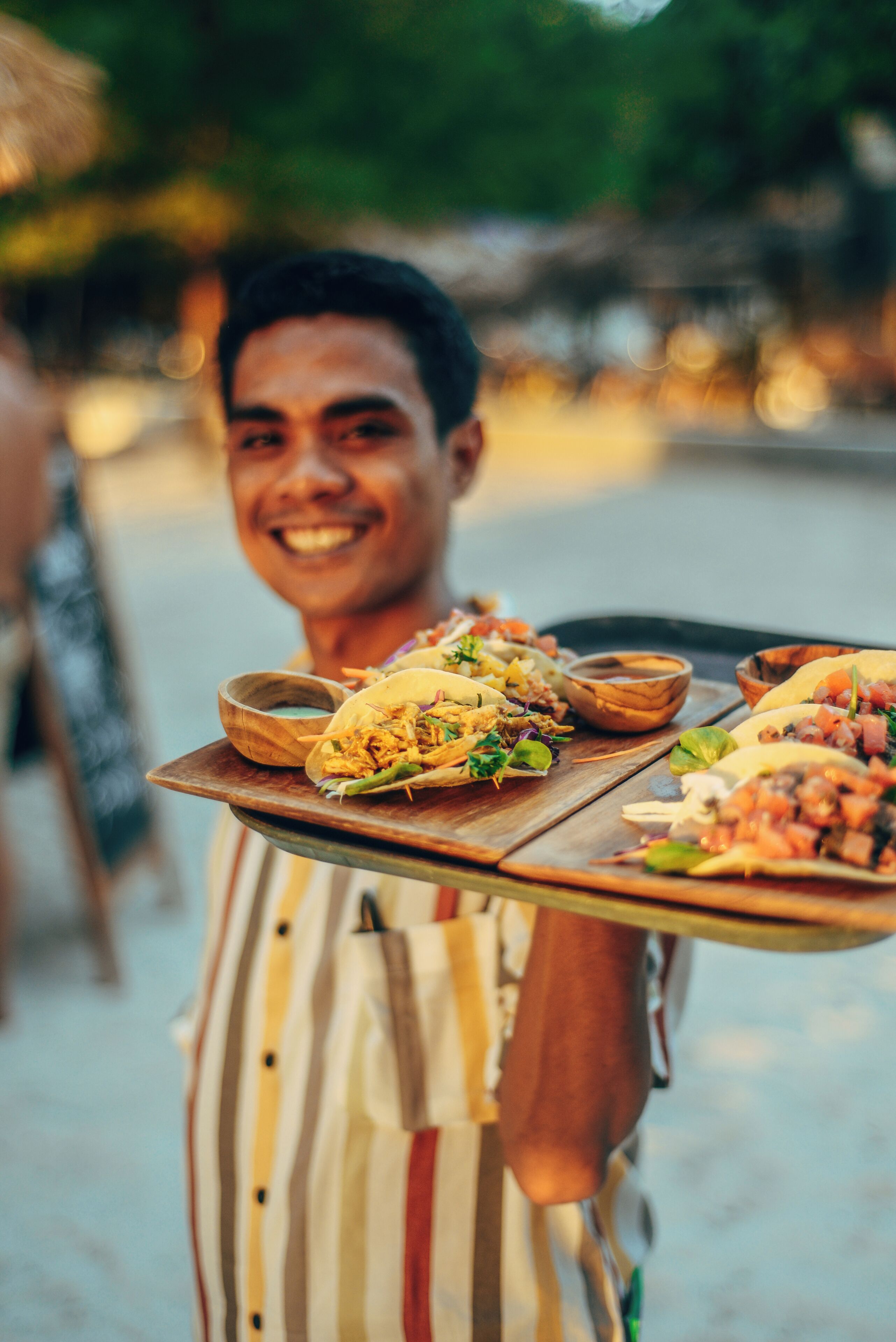 A person carrying a tray with tacos and bowls of sauce.