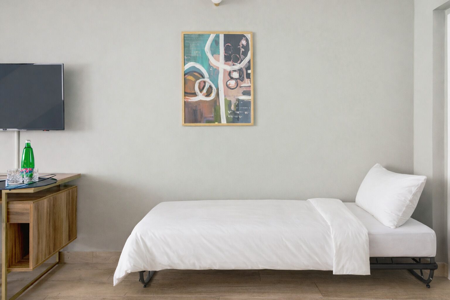 A minimalist room with a bed, a TV, and a painting on the wall.