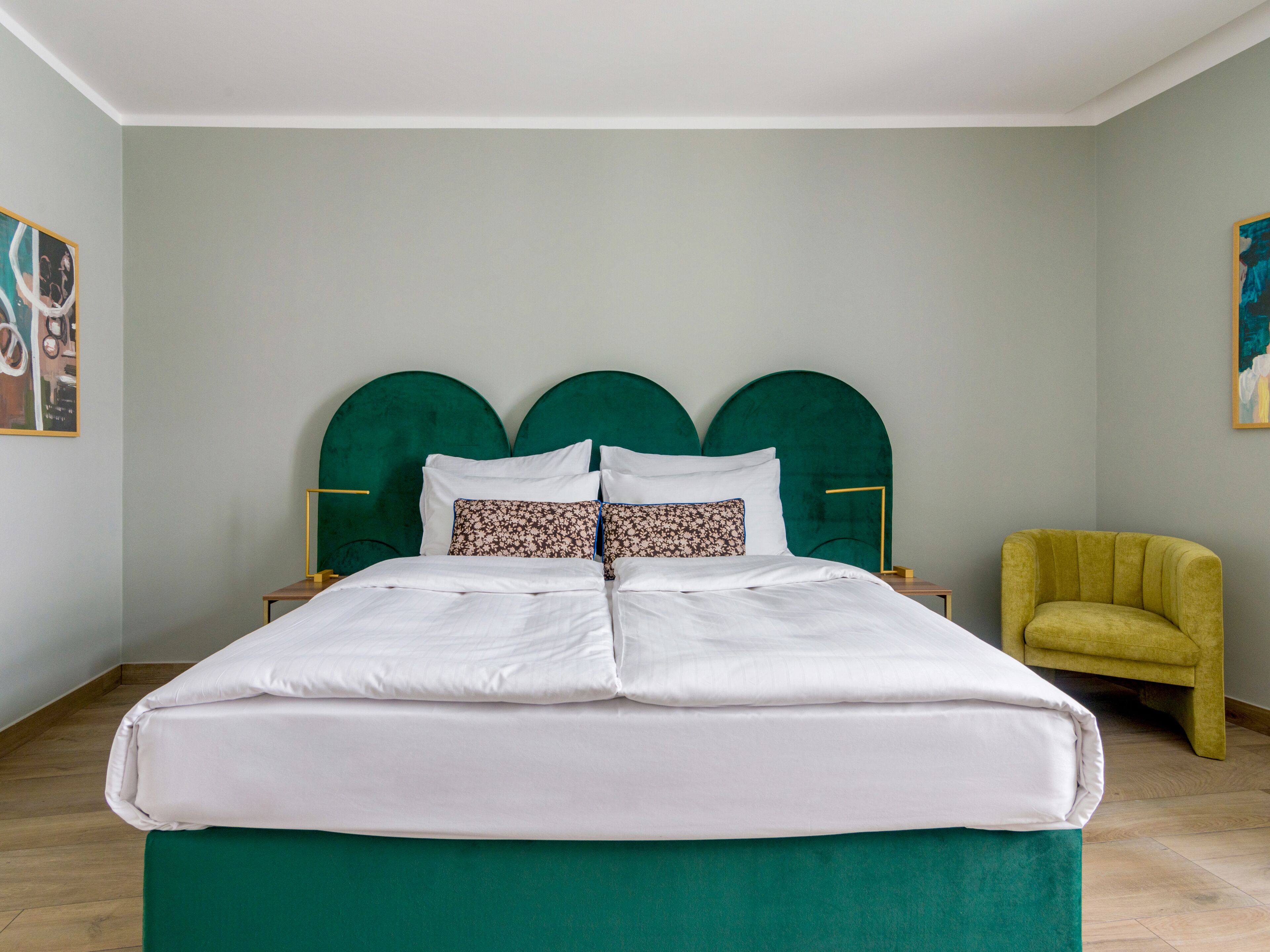 Un letto rifatto con lenzuola bianche e una testiera imbottita verde.