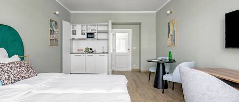 A hotel room with a bed, a desk, a chair, a kitchenette, and a TV.