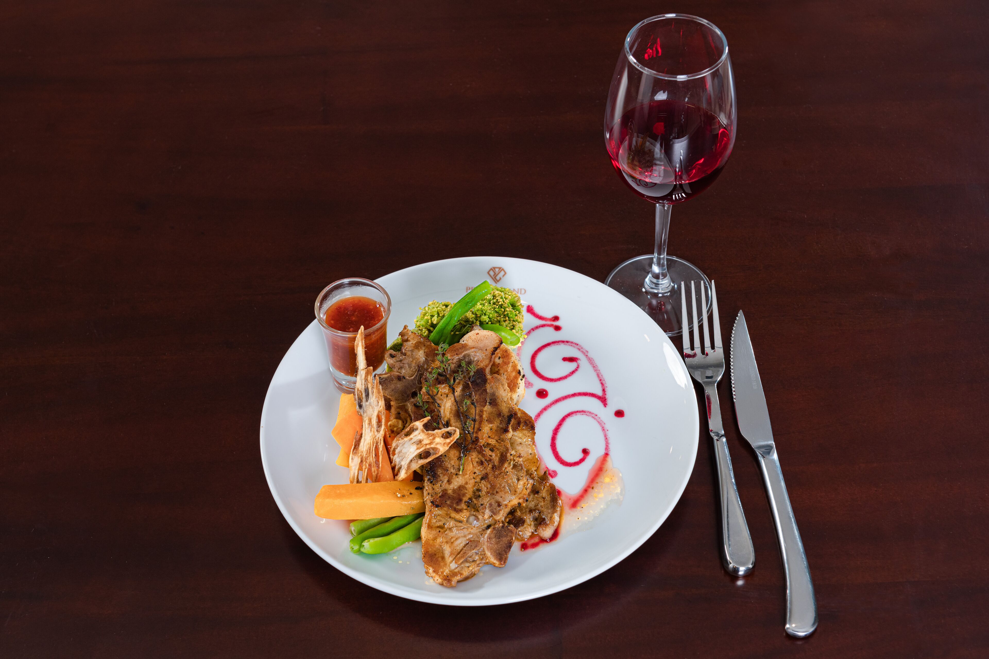 A plate of food with a glass of red wine and cutlery on a wooden table.