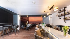 A modern bar area with wicker furniture, a bar counter, and a sunset view through the open space. - Pearl Grand By Rathna (Colombo)
