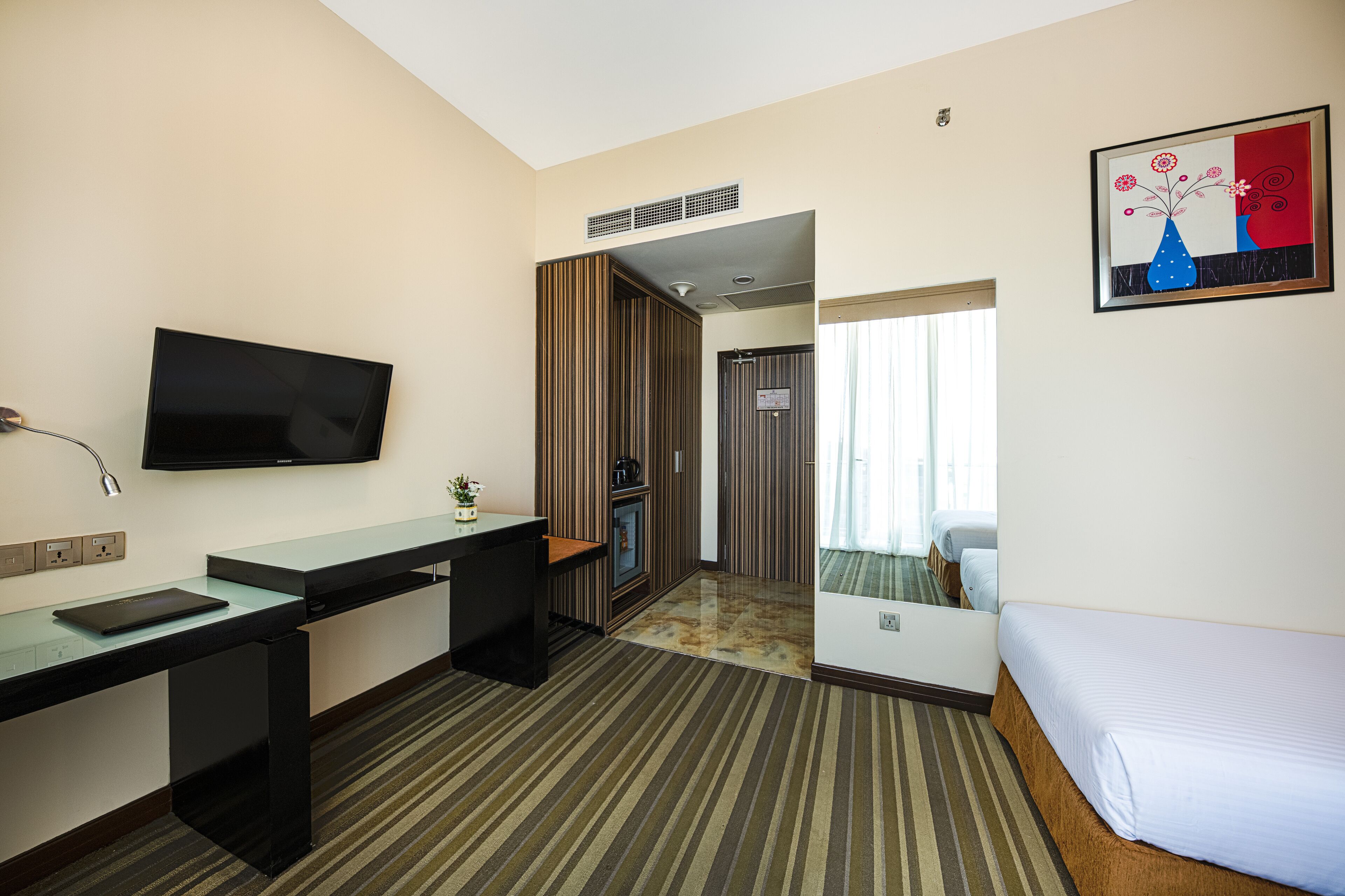 A hotel room with a bed, a desk with a computer, a television, and a bathroom visible through a door.