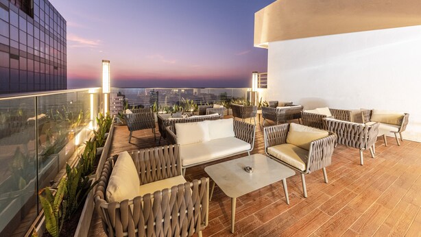 A rooftop terrace with outdoor seating, a glass balustrade, and a city view at dusk. - Pearl Grand By Rathna (Colombo)
