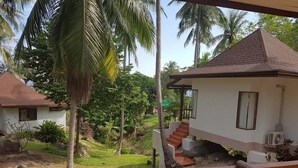 A wooden deck with a table and chairs, overlooking a garden with palm trees and a small building with a red roof. - Diamond Beach Resort (Koh Tao)