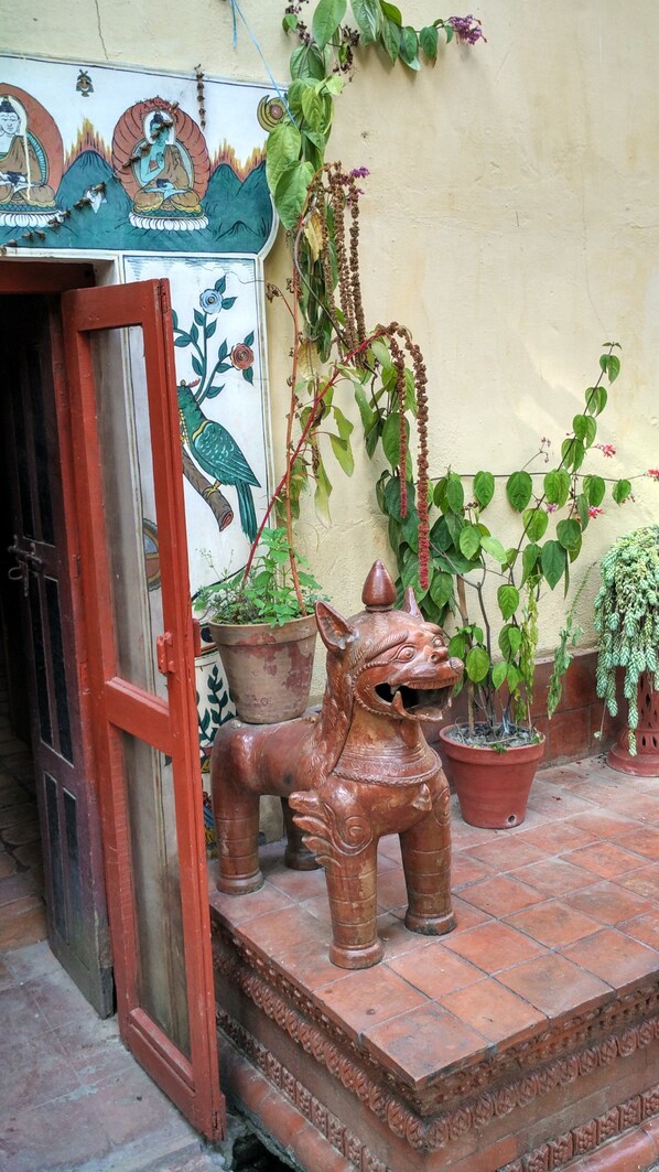 A traditional door with a red frame, a decorative wall with a mural, and several potted plants including a large terracotta animal figure. - Hotel Vajra (Kathmandu)