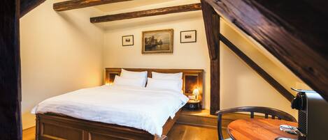 A bedroom with a wooden bed, a nightstand with a lamp, and a small table with a coffee machine.