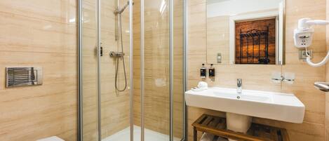A modern bathroom with a glass-enclosed shower, a white sink, and a wooden shelf with towels.