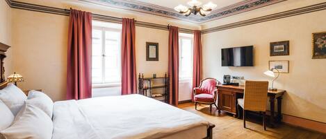 Een hotelkamer met een groot bed, een bureau met stoel, een televisie en een boekenkast.
