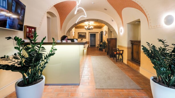 Um saguão de hotel com balcão de recepção, plantas em vasos, um candelabro e tetos em arco.