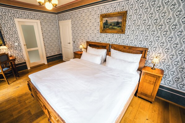 A neatly made bed with white linens in a room with patterned wallpaper and wooden flooring. - Hotel Latrán (Cesky Krumlov)