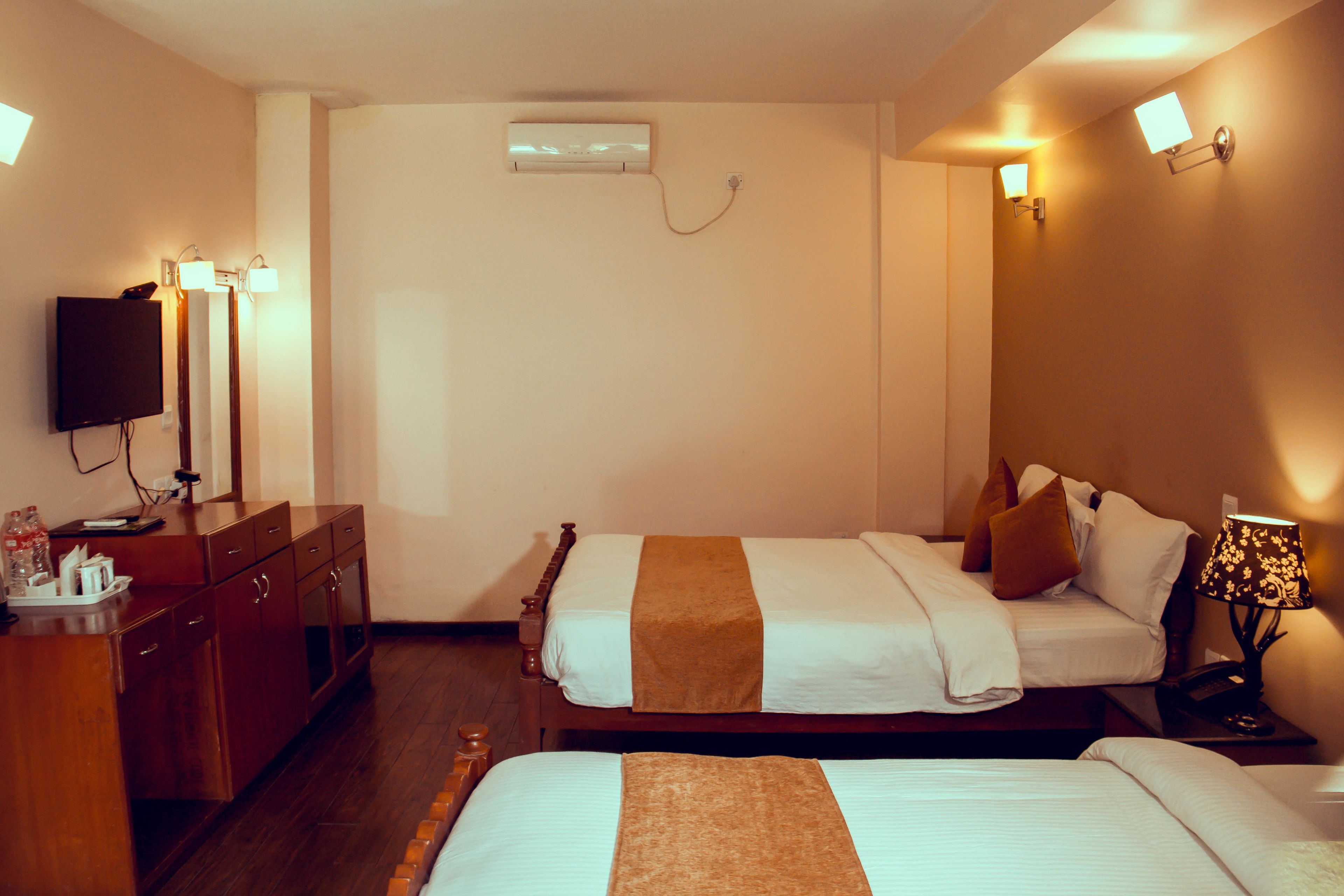 A hotel room with two beds, a TV, a desk with a lamp, and a wall-mounted air conditioner.