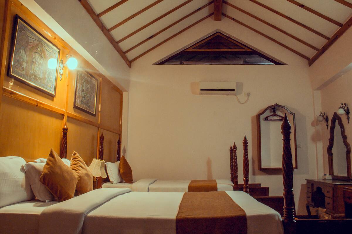 Une chambre d’hôtel avec deux lits, un plafond en bois, un appareil de climatisation, un miroir et une lampe.