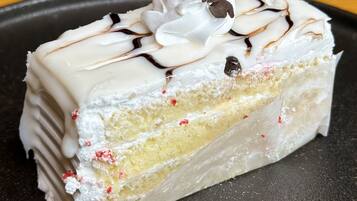 A slice of layered cake with white frosting, chocolate drizzle, and chocolate chips on a black plate.