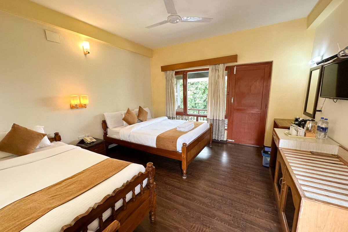 Une chambre d’hôtel avec deux lits en bois, un ventilateur de plafond, un bureau en bois avec un miroir et une fenêtre avec des rideaux.