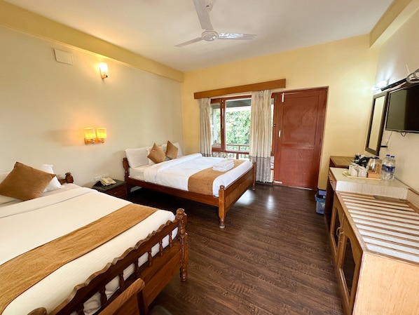 A hotel room with two wooden beds, a ceiling fan, a wooden desk with a mirror, and a window with curtains.