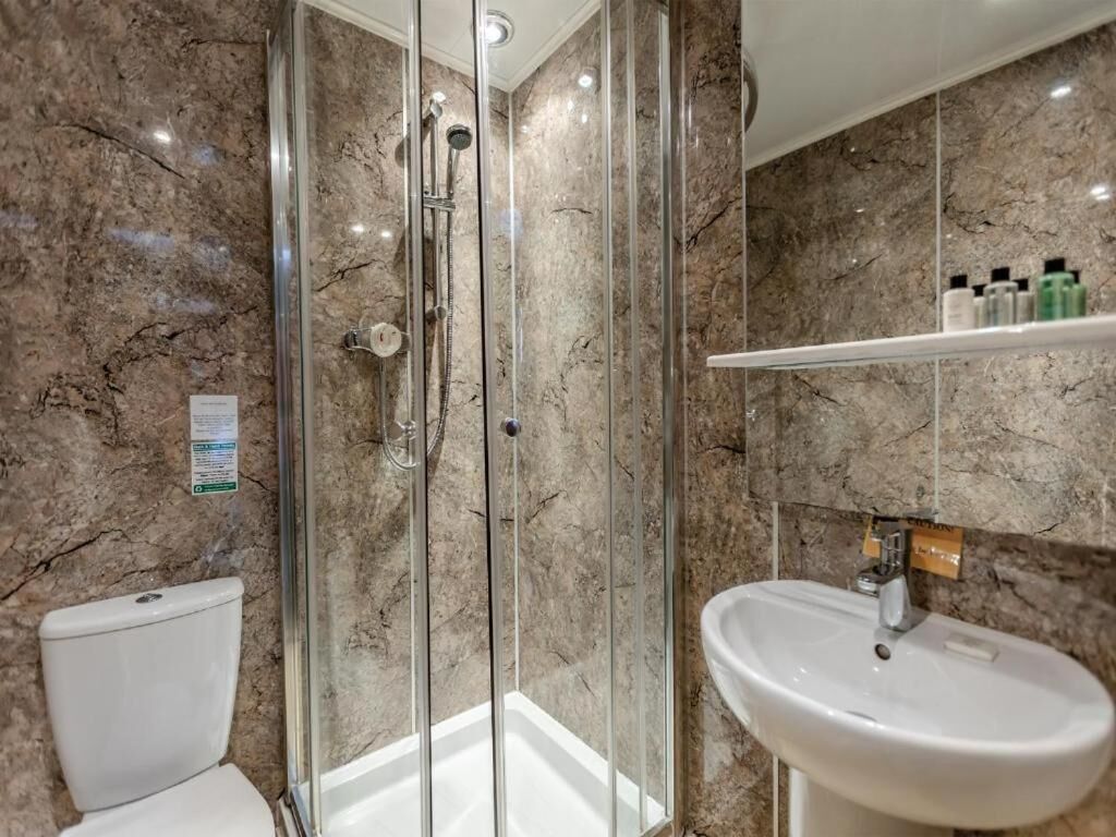A bathroom with a glass-enclosed shower, a white sink, and a marble-tiled wall.