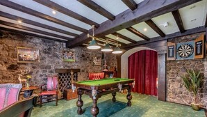 A billiards room with a pool table, wooden chairs, a dartboard, and a stone wall. - The Tormaukin Hotel (Dollar)