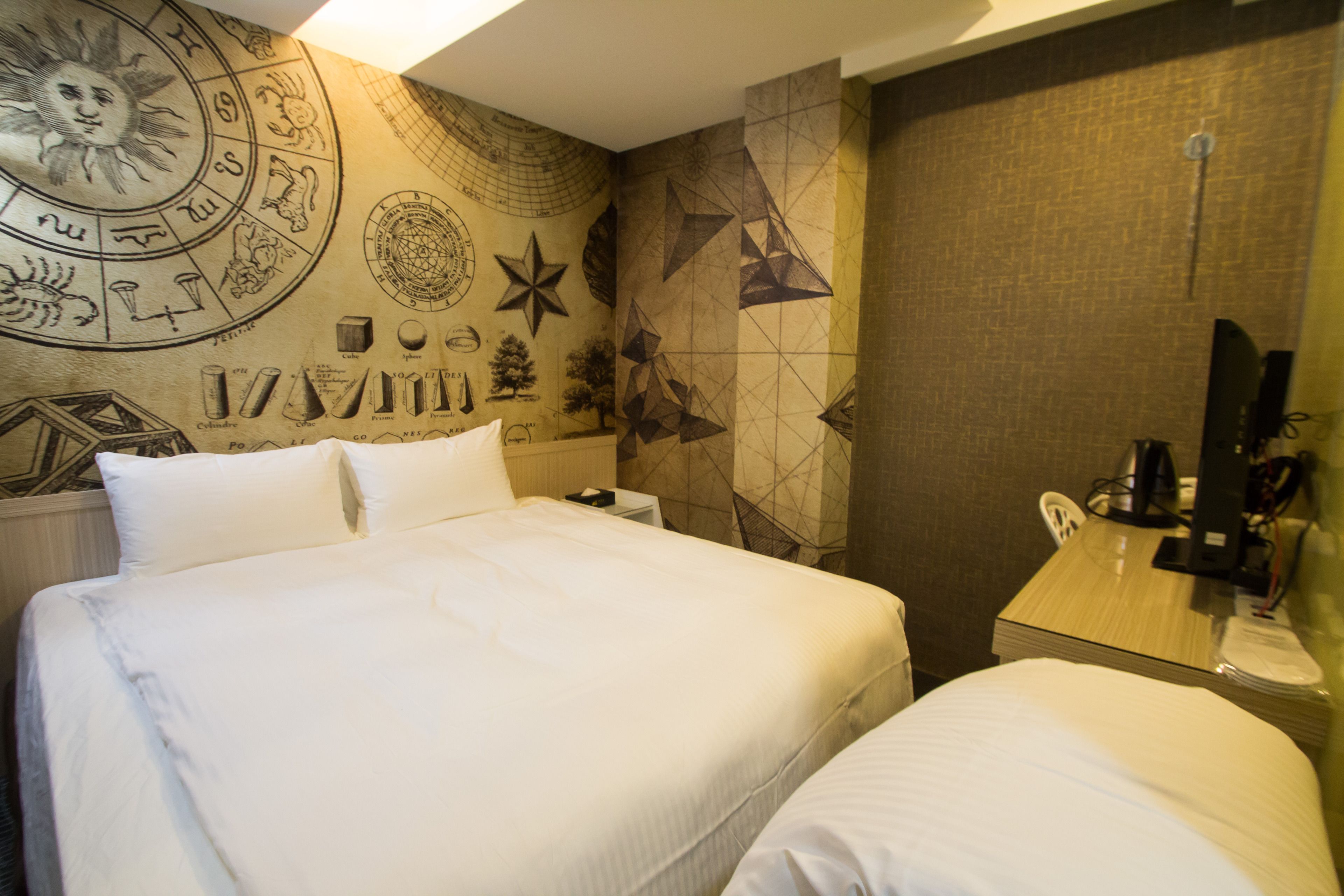 Ein Hotelzimmer mit einem großen Bett, einem Schreibtisch und einer Wand, verziert mit geometrischen Mustern und Tierkreiszeichen.