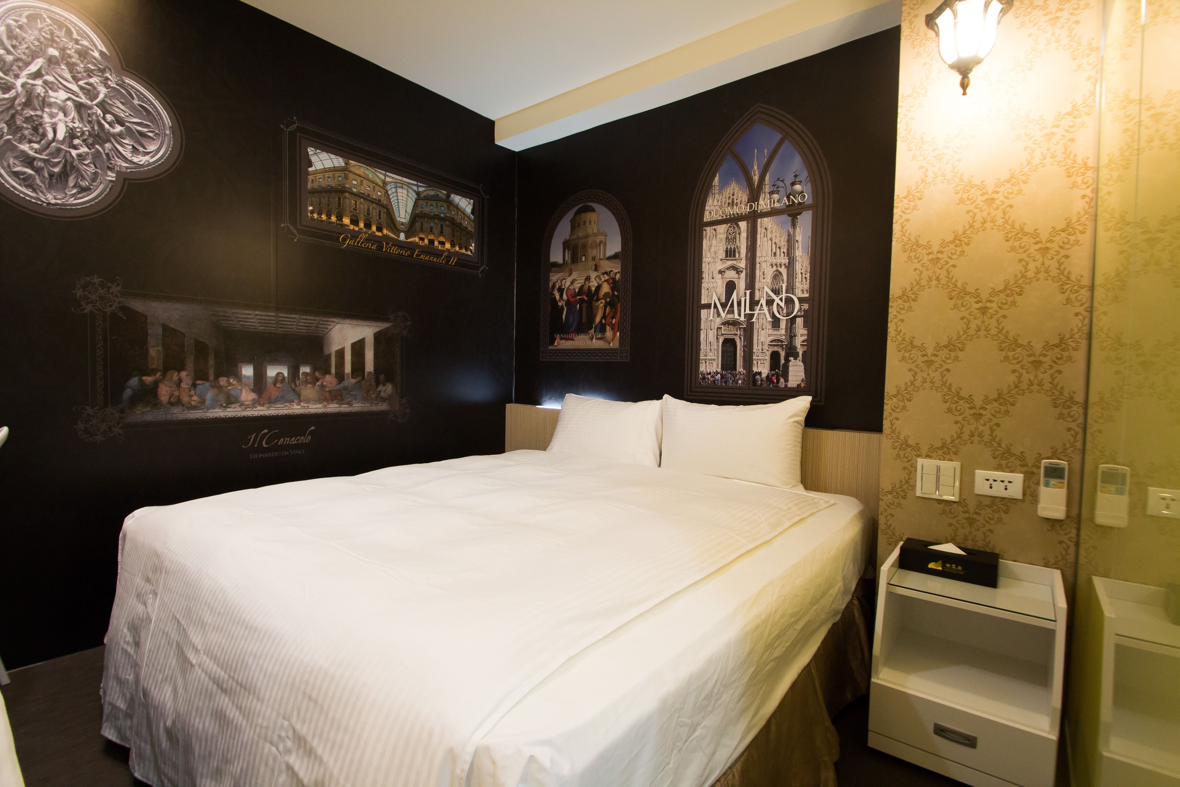 Una habitación de hotel con una cama grande, una mesita de noche, una pared con detalles artísticos y una ventana.
