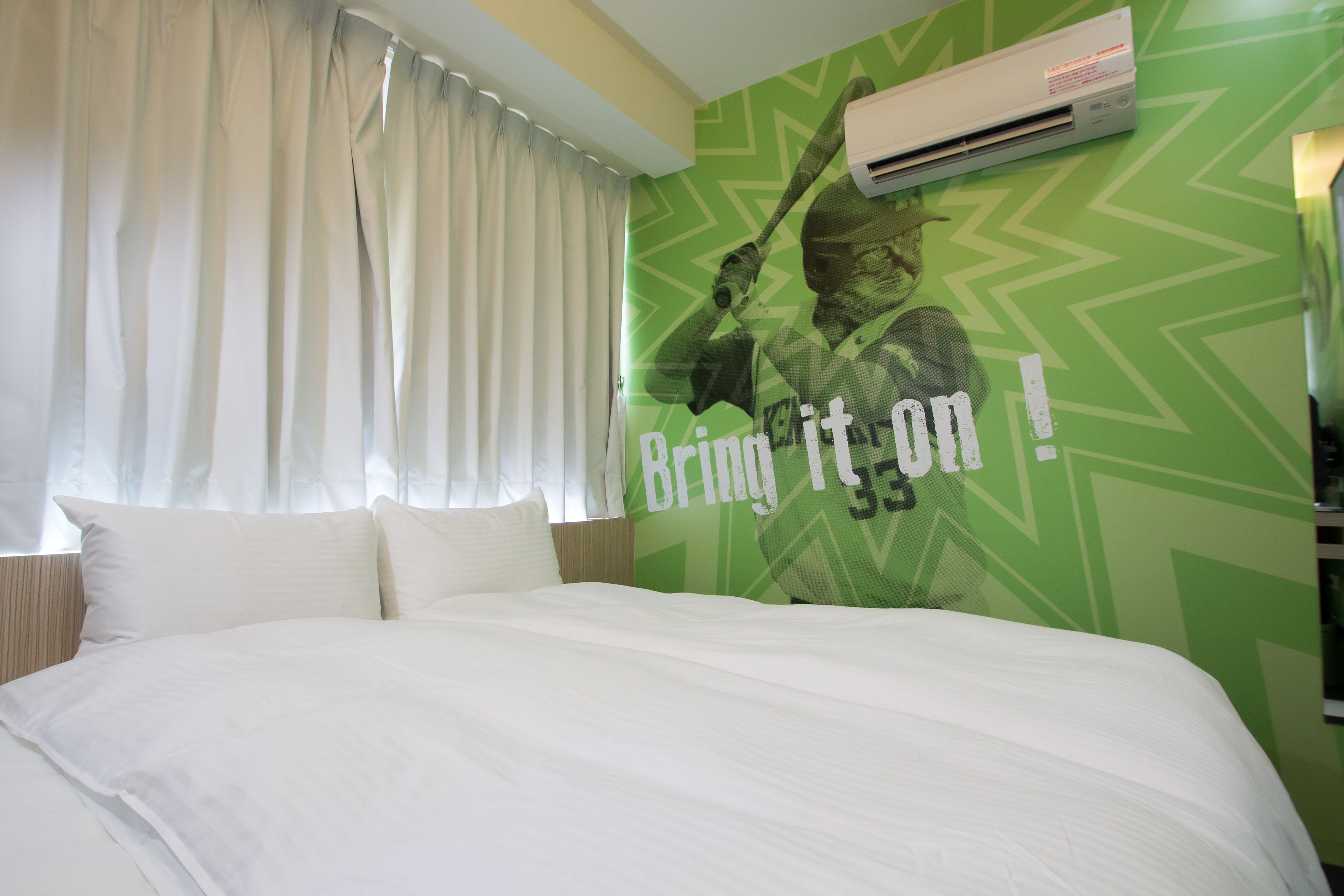 A hotel room with a bed, white curtains, and a green wall with a graphic.