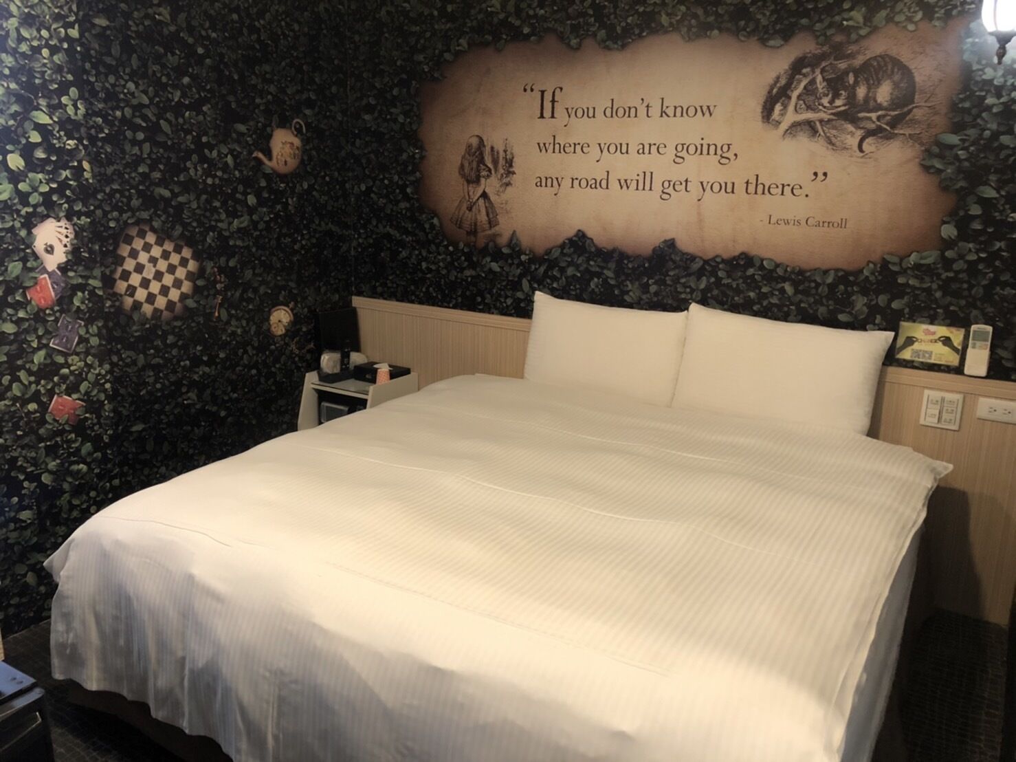 A bedroom with a bed, a nightstand, a wall with a quote, and a clock.