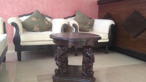 A room with a sofa set against a pink wall, a round wooden table with carved legs, and a dark wooden cabinet. - De Hotel Veda (Kathmandu)