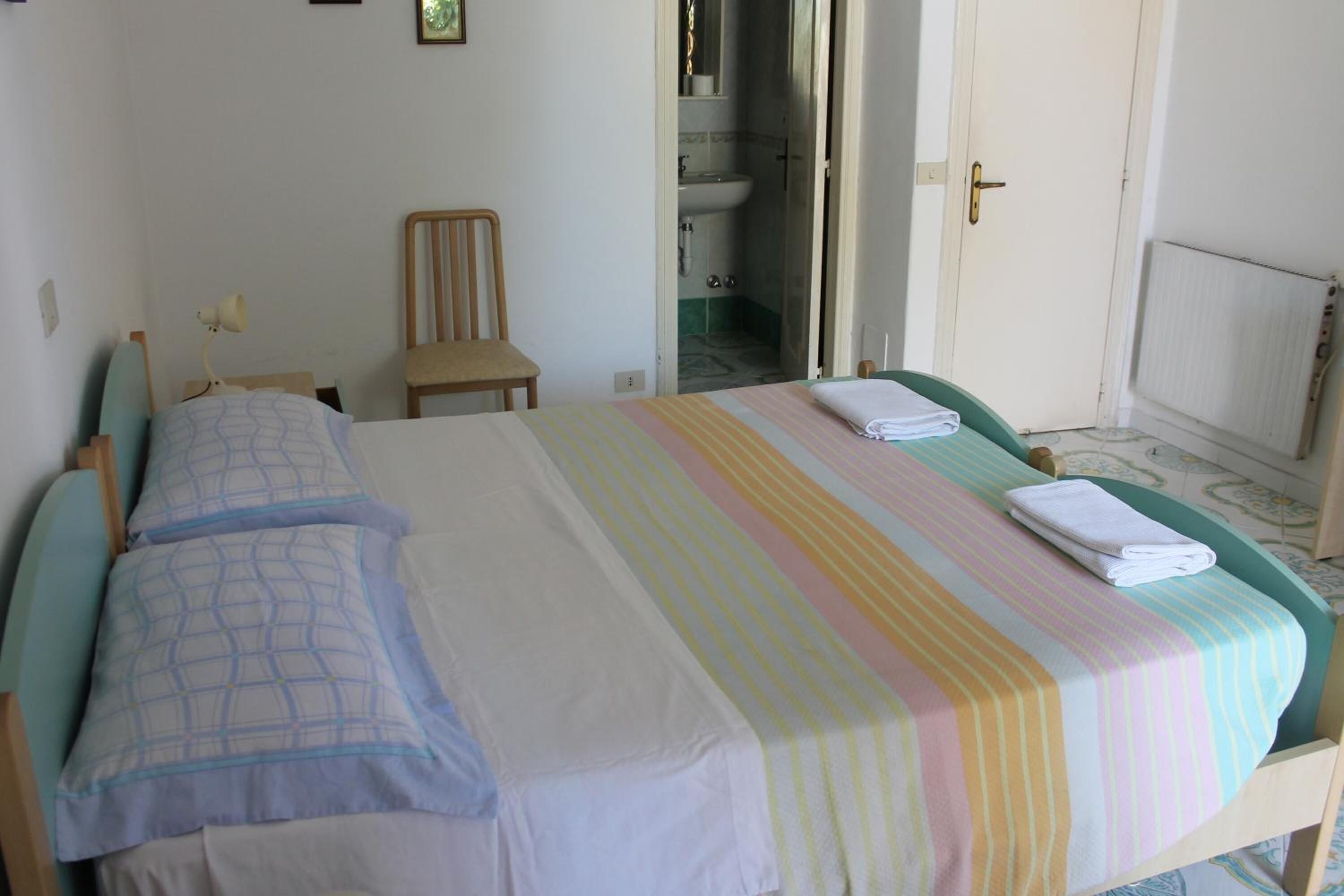 Une chambre avec deux lits, une chaise et une salle de bain visible à travers une porte ouverte.