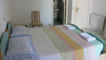 Une chambre avec deux lits, une chaise et une salle de bain visible à travers une porte ouverte.