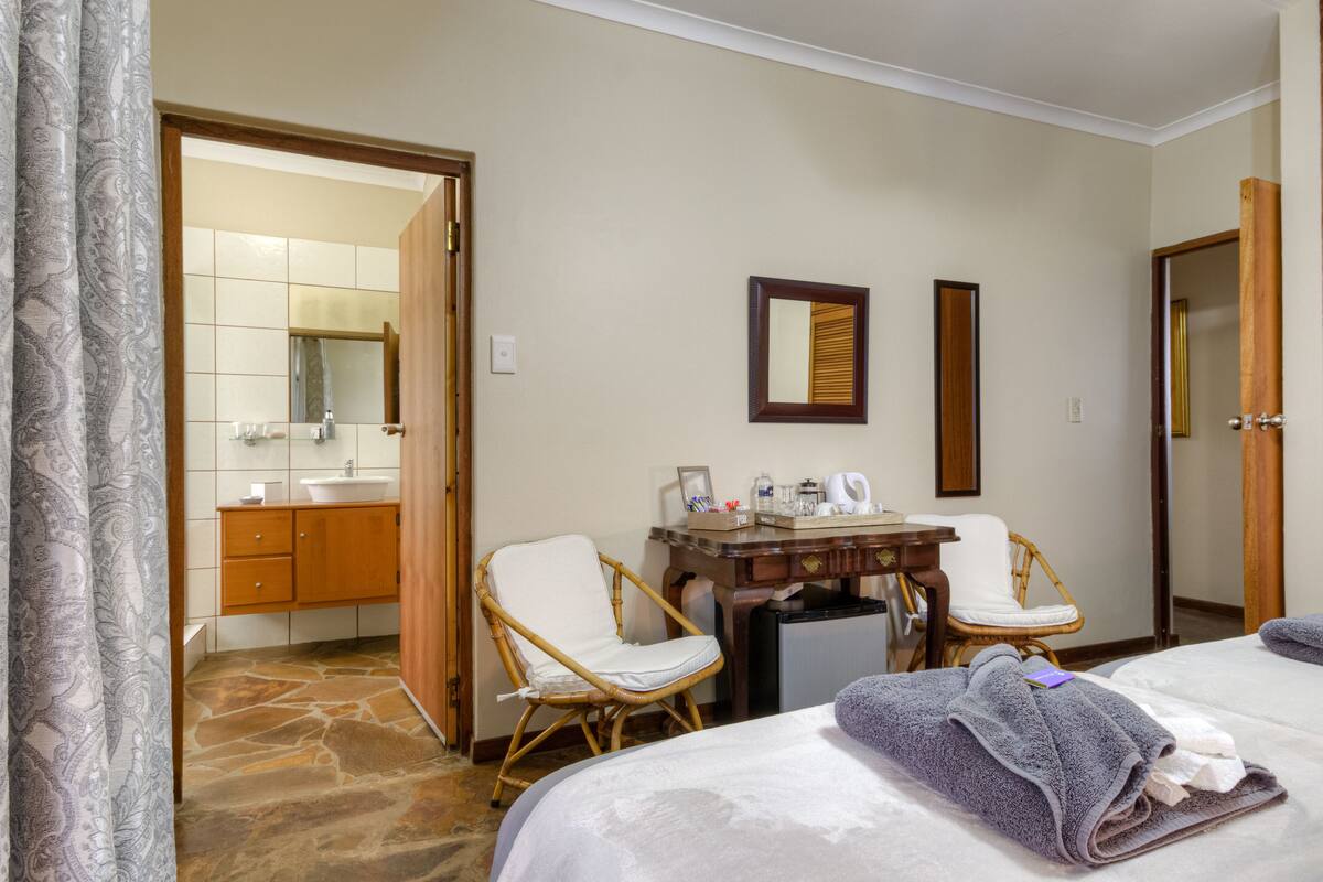 A hotel room with a bed, a small table with chairs, a bathroom with a sink and mirror, and a door leading to another room.