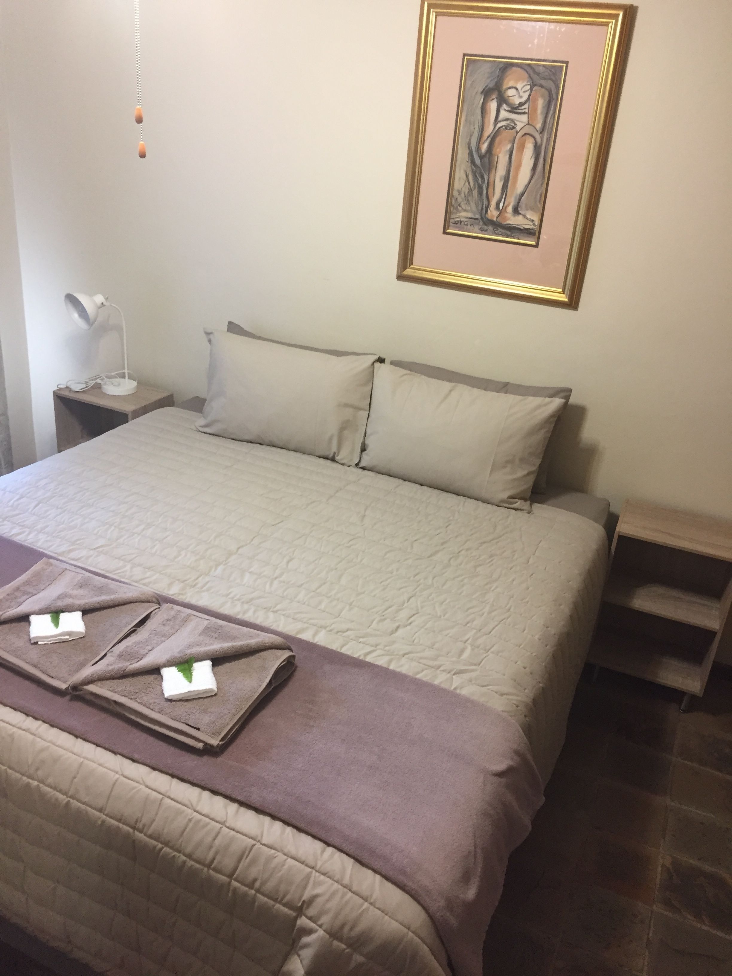 Un lit bien fait, recouvert d’une couette beige, de deux oreillers et d’une couverture marron. Un tableau encadré est accroché au mur, au-dessus du lit.