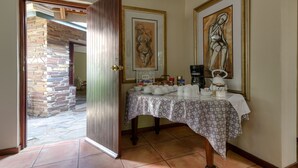 Una habitación con pared de piedra, puerta de madera, una mesa con mantel estampado y dos obras de arte enmarcadas.